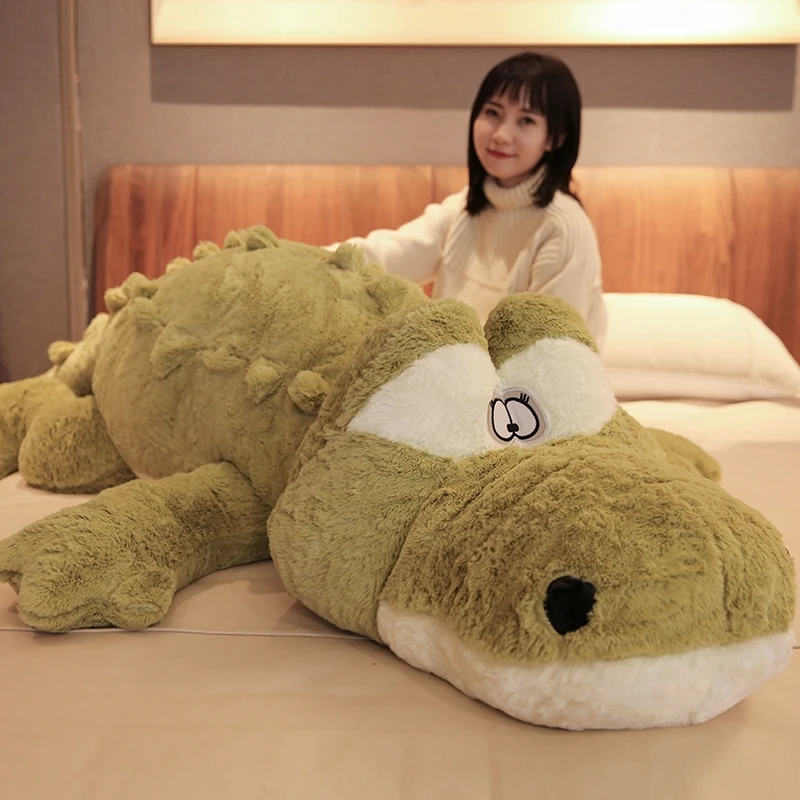 Alligator gosedjur i stor kuddform, söt design med realistiskt fjällmönster, 200 cm 22 Stor olivbrun krokodilformad plysch på en säng bredvid en person.