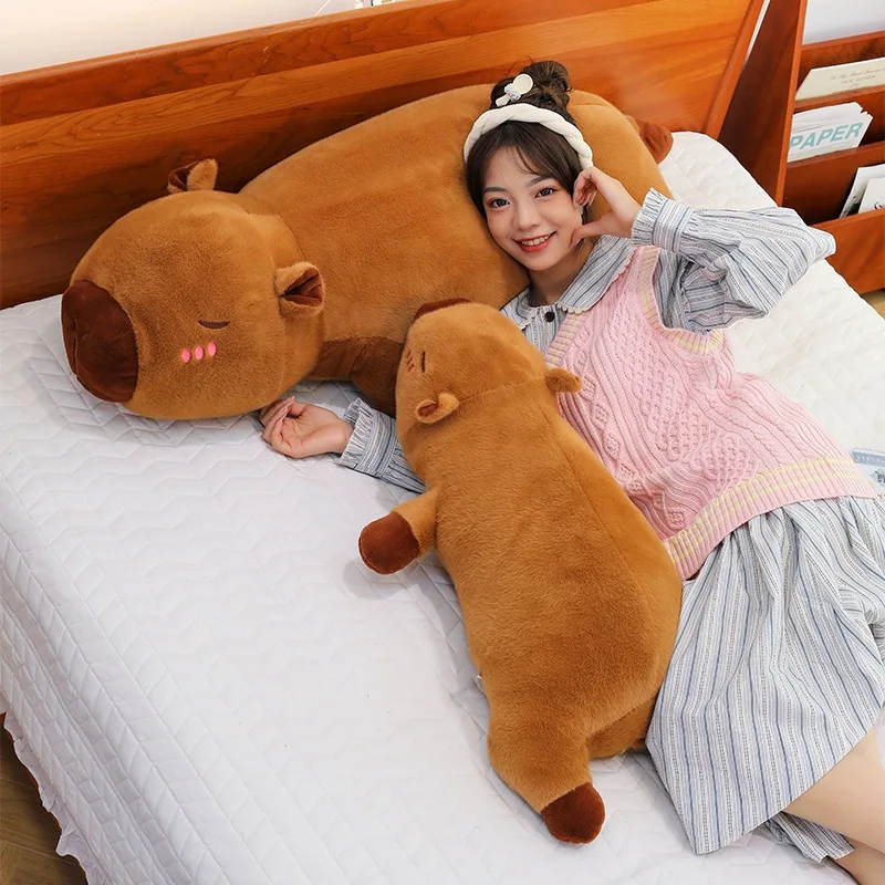 Kawaii kapybara gosedjur som mjuk, fluffig sovkudde för soffan, skolan och tupplur 22 En person vilar på en säng med stora mjuka plyschdjur.