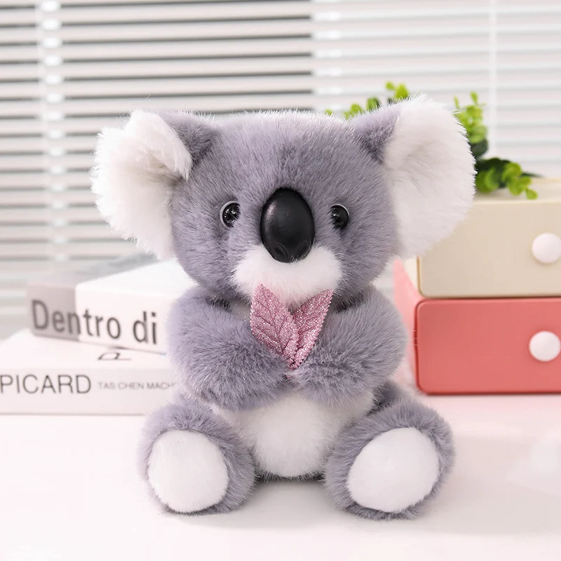 Koala plyschkudde med sött lövmönster, mjuk sovkompis från Australien, 22 cm 21 Sittande grå och vit koala med rosa rosett, fotograferad framifrån.