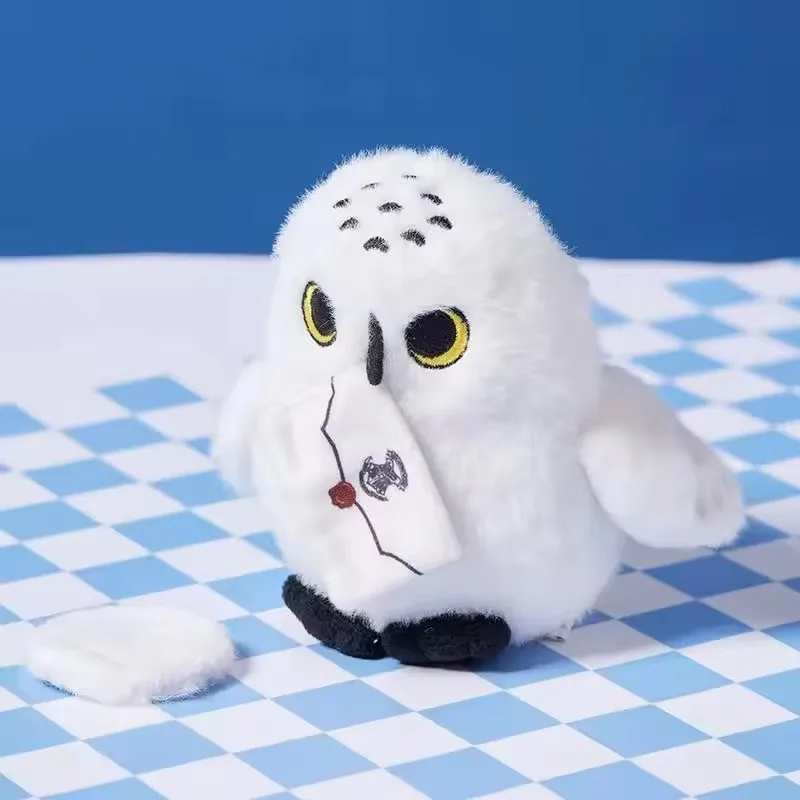 Hedwig uggla gosedjur, mjuk snöuggla utformad som axelprydnad med lekfull design 20 Visa den vita uggleplyschen sittande snett på ett blått och vitt rutigt underlag.