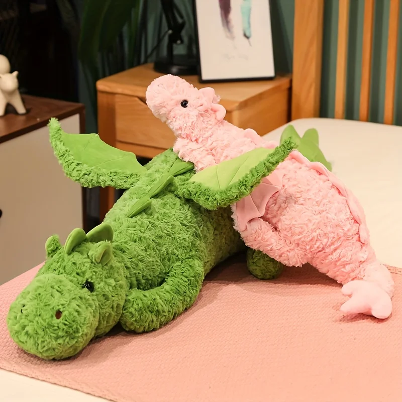 Dinosaurie gosedjur som flygande drake, två färgval som födelsedagspresent till vänner 22 Två mjuka gosedjur i drak- och dinosaurieform, ett grönt och ett rosa, placerade på en säng.