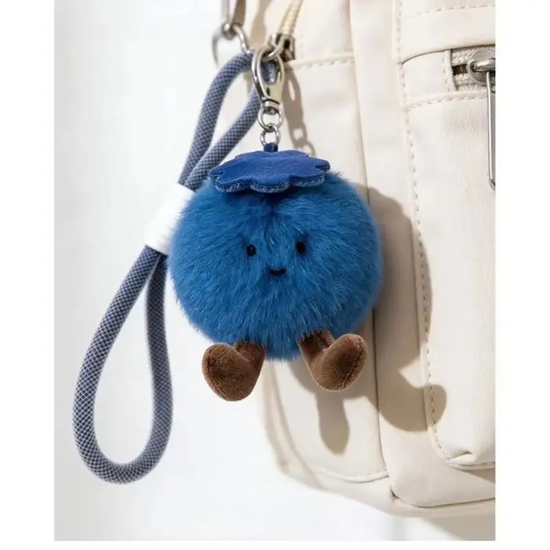Nyckelring med blåbärsdesign, fluffig lyckobringare och flera figurvarianter 21 Blåbärsberlocken hänger från en vit väska med remmen synlig.