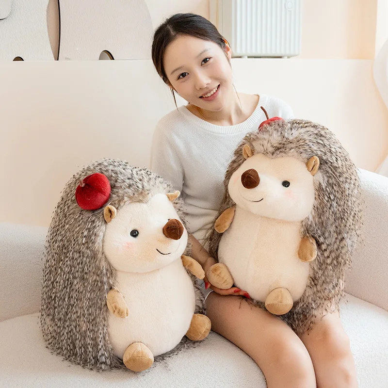 Hedgehog som plyschkudde, Chubby och kawaii, rund hedgehogmotiv long haired, 23–43 cm 22 Två gråbruna igelkottsgosedjur med ljusa magar sitter bredvid en person.