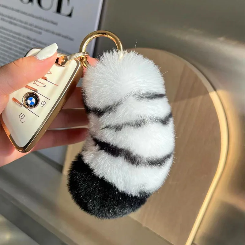 Kanin som nyckelring, Snow leopard print och söt, 12–15 cm 22 Vit och svart pälssvans med guldfärgad nyckelring bredvid en mobiltelefon och handväska.