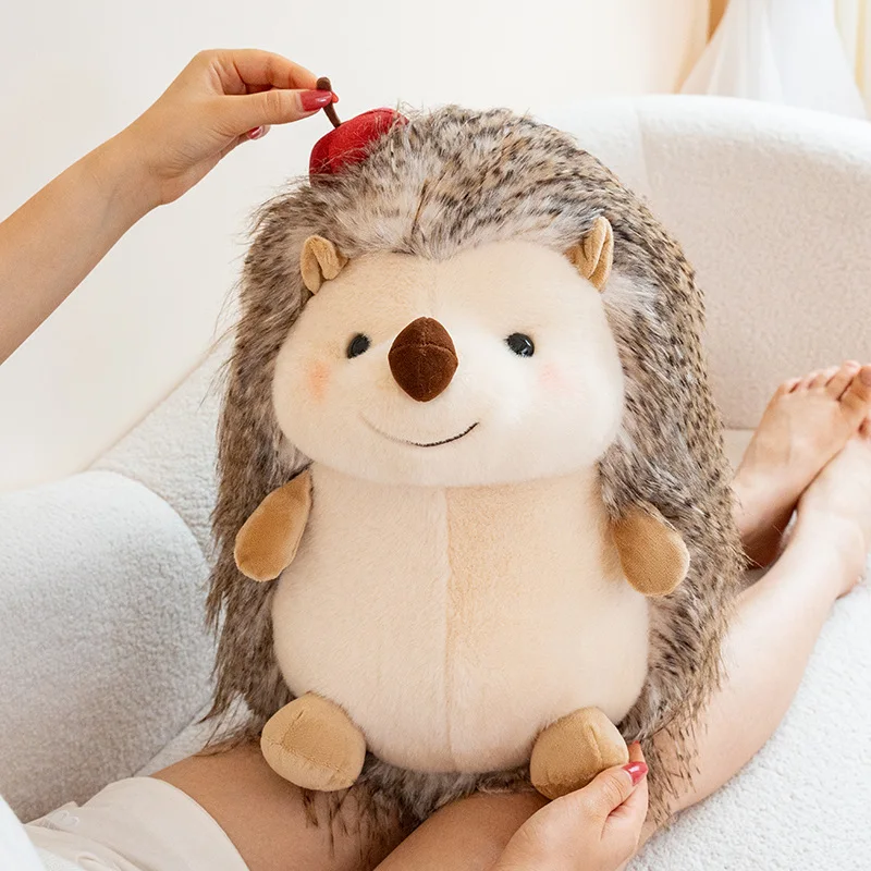 Hedgehog som plyschkudde, Chubby och kawaii, rund hedgehogmotiv long haired, 23–43 cm 23 Närbild av ett gråbrunt igelkottsgosedjur med ljus mage, sittande i ett knä.