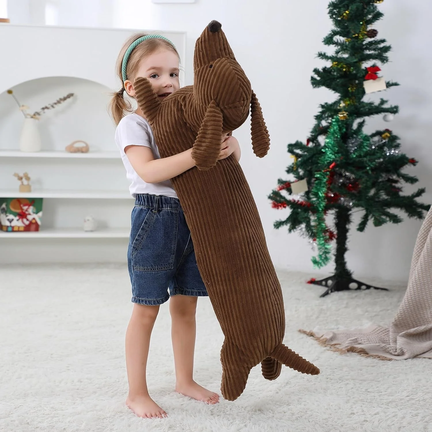 Dachshund som hundgosedjur, lång kroppskudde med söt och rolig stil, 50–110 cm 18 Brun, lång hundplysch hålls av ett barn i ett rum med julgran.