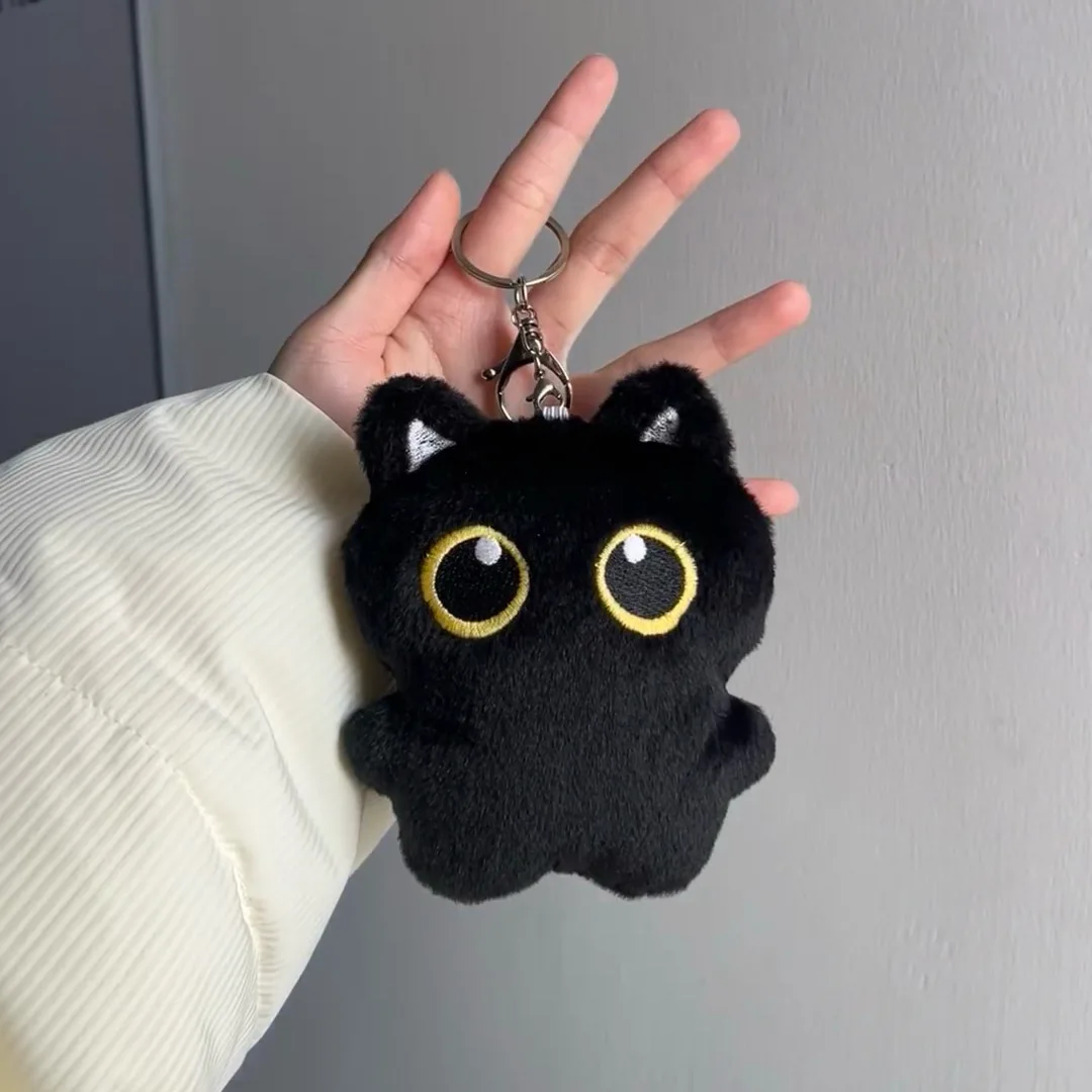 Tecknat svart kattgosedjur med pipfunktion, nyckelring och hänge till väskan 21 Svart kattnyckelring med gula ögon visad i en hand.