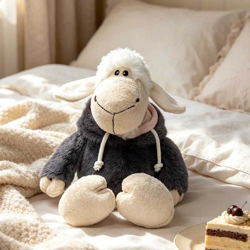 Får och lamm gosedjur, Wearing clothing och Described as high quality, 30–36 cm 19 Visa fårgosedjuret sittande i svart klädsel mot en ljus bäddmiljö.