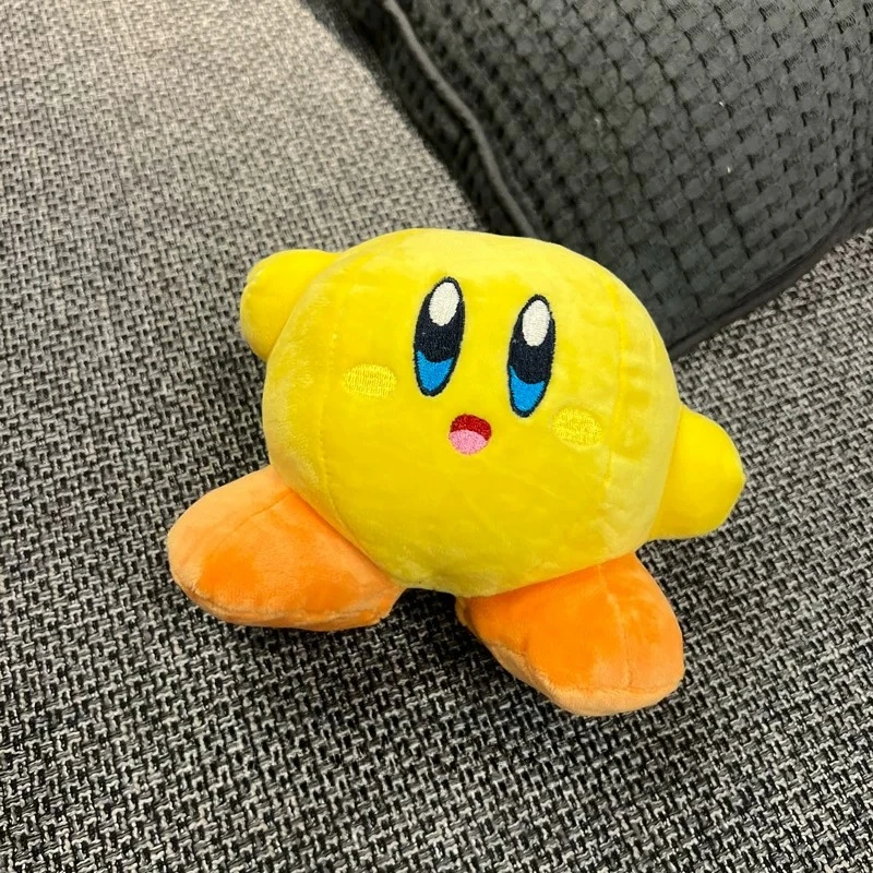 Samlarfigur i form av en orange Kirby-docka med arg min och tecknad spelstil 81 Den gula karaktärsplushen med orange fötter visas på ett mörkt, vävt underlag.