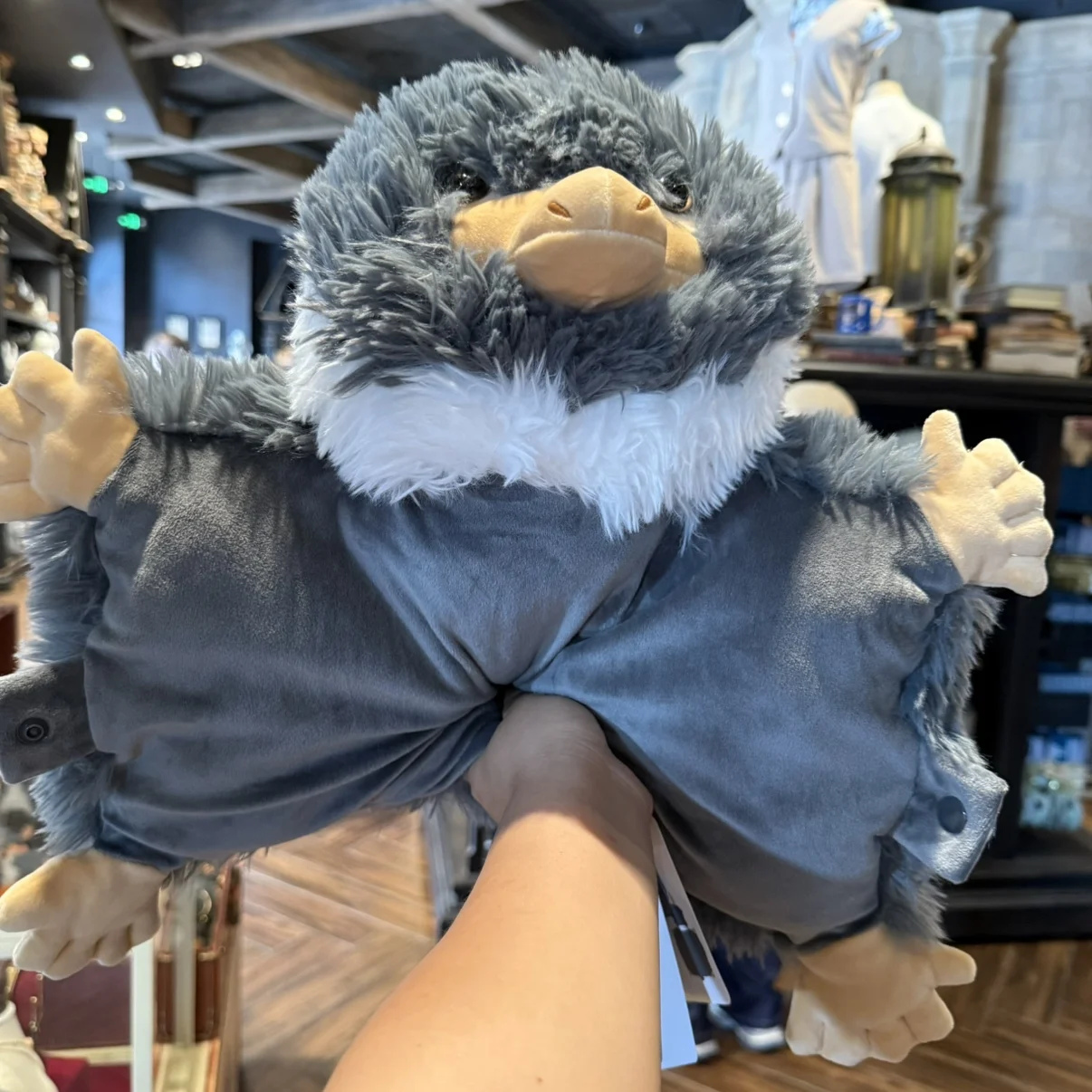 Niffler gosedjur som plyschkudde och karaktärsdocka, souvenir från Fantastic Beasts 20 Lurvig grå Nifflerfigur med utsträckta armar och gulorange detaljer.