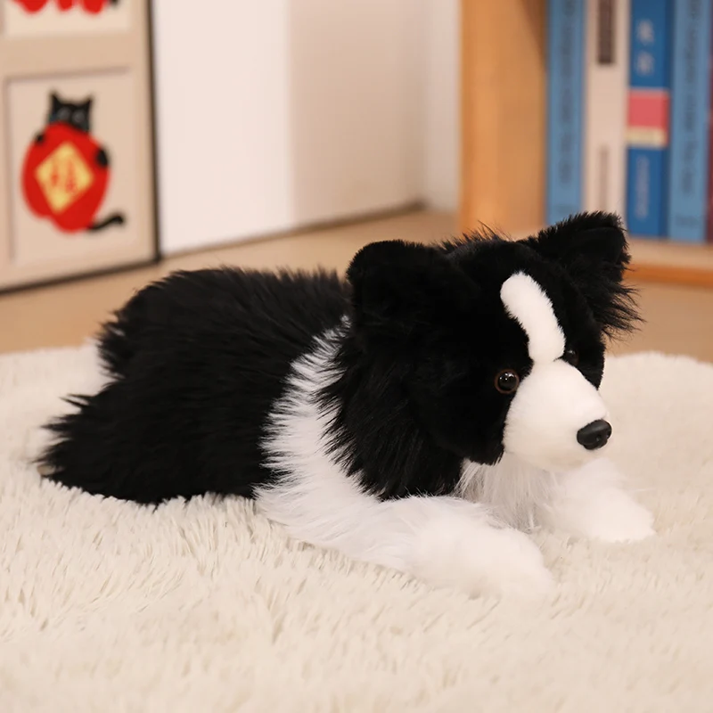 Realistisk hundleksak föreställande Border Collie, med naturtrogen form och detaljer 22 Svartvit hundplysch ligger på en ljus matta.